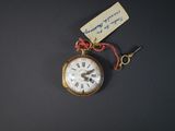 une petite montre de poche en or à laquelle est attachée une étiquette
