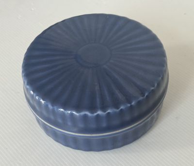 un petit récipient bleu muni d'un couvercle, posé sur une table