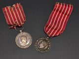 two medals on a black surface with a red and white striped ribbon