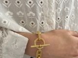 someone wearing a white shirt and a gold bracelet with a knot