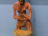 une statue en bois représentant un homme assis sur un tabouret