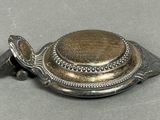 a silver plate with a metal lid on a gray surface