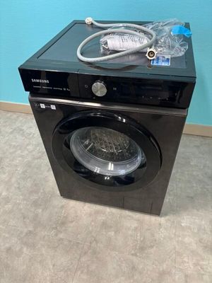 une machine à laver noire sur laquelle est posée une bouteille d'eau, devant un mur bleu