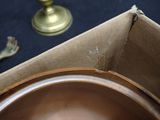 a metal bowl sitting in a box next to a gold candle