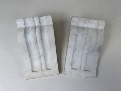une paire de serre-livres en marbre blanc posés sur une surface blanche