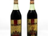 two bottles of red wine sitting next to each other on a white surface