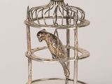 un oiseau en argent dans une cage posée sur un socle