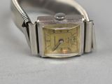 a silver wrist watch with a yellow face on a white surface