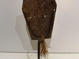 a wooden mask on a metal stand with a piece of wood sticking out of it