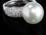 une photo d'une bague en perle et diamant posée sur un fond noir