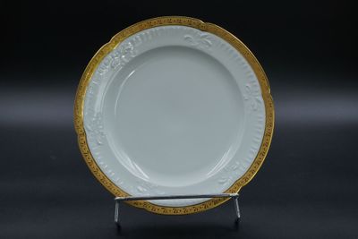 une photo d'une assiette blanche bordée d'or, posée sur un socle