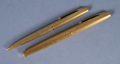 two golden colored pens sitting next to each other on a blue surface