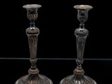 une paire de bougeoirs en argent posés sur une table en verre, sur fond noir