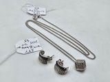two pieces of silver jewelry sitting on top of a white table