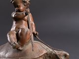 bronze figurine of a child on a turtle on a black background