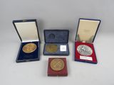 trois médailles d'or et d'argent sont exposées dans un coffret posé sur un support blanc