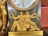 a gold clock on a marble table with a statue of a man holding a sword