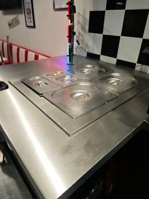 un plan de travail en acier inoxydable équipé de quatre feux, dans une cuisine aux murs à carreaux