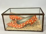 pair of orange shoes in a glass box on a bed of pearls