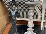 une statue représentant un garçon tenant un bac à oiseaux posé sur une table à côté d'une chaise