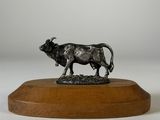 statue d'un taureau posée sur un socle en bois, sur fond blanc