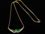 a gold necklace with a green stone on a black background