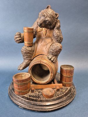 une statue représentant un ours assis sur un tonneau, tenant une tasse