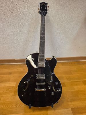 a black electric guitar sitting on a hard wood floor