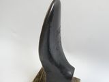 un objet noir posé sur un socle en bois, près d'un mur blanc