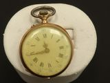 une montre de poche en or posée sur un socle blanc