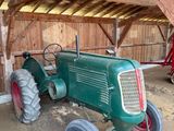 un tracteur vert garé dans une grange, avec un tracteur rouge derrière lui