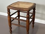 un vieux tabouret en bois avec une assise en osier, posé sur un sol gris