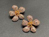 two gold tone flower earrings with pink crystals on a black surface