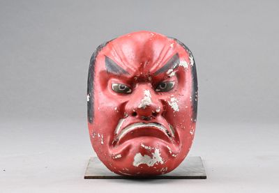 un masque rouge posé sur un socle, sur fond gris