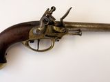 un vieux revolver en laiton avec une crosse en bois, posé sur une surface blanche