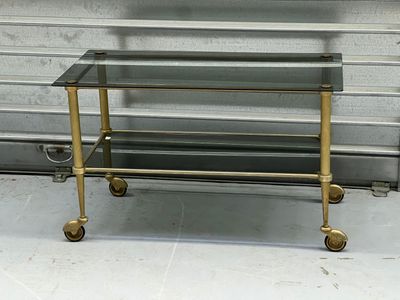 une table basse en verre et en laiton, posée au sol et munie de roulettes