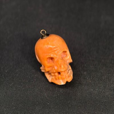 un pendentif en forme de crâne sculpté de couleur orange, muni d'un cordon noir, sur fond noir