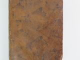 an old brown book sitting on top of a table next to a white wall