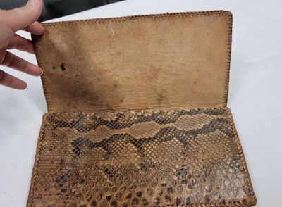 Quelqu'un tient un portefeuille orné d'un motif en peau de serpent.