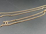 two gold chains on a black surface with a gold clasp
