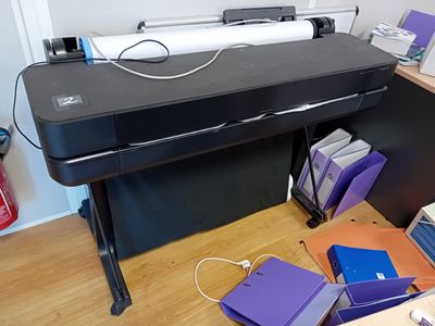 une grande imprimante noire posée sur un bureau, à côté d'un ordinateur portable