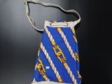 un sac à main bleu et jaune muni d'une anse en corde, sur un fond noir