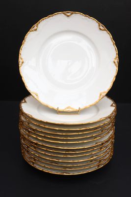 une pile de six assiettes blanches et dorées posées sur une surface noire