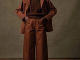 une photo d'une femme en tailleur marron, debout sur un parquet