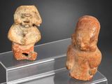 deux figurines en pierre représentant un homme et une femme, posées sur des socles en acrylique
