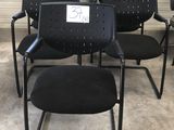 Plusieurs chaises noires sont alignées en rangée, avec une pancarte fixée sur le dossier.