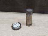 a small silver pocket watch next to a lighter on a table