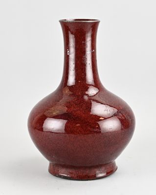 un vase rouge posé sur une surface blanche