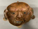 a close up of a bronze mask on a white surface