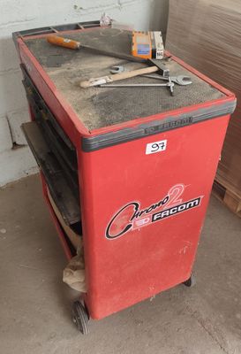 une glacière rouge posée dans un garage, avec des outils dessus